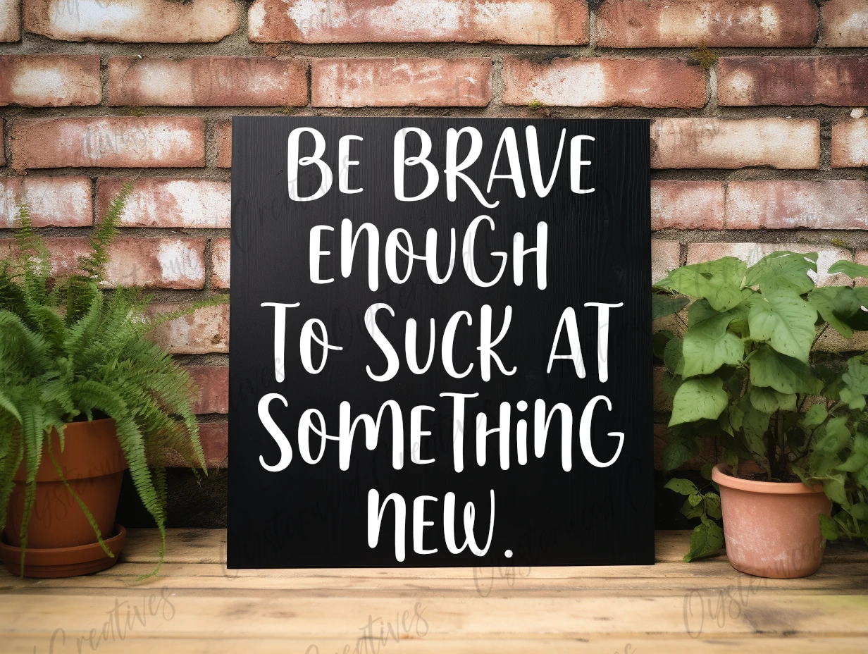 Be brave enough to suck at something new. Black sign with white lettering.