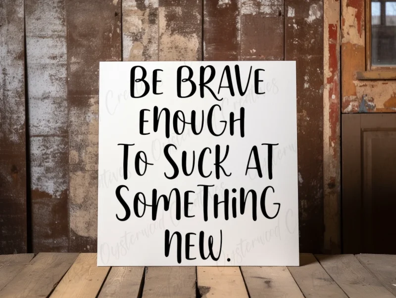 Be brave enough to suck at something new. White sign with black lettering.