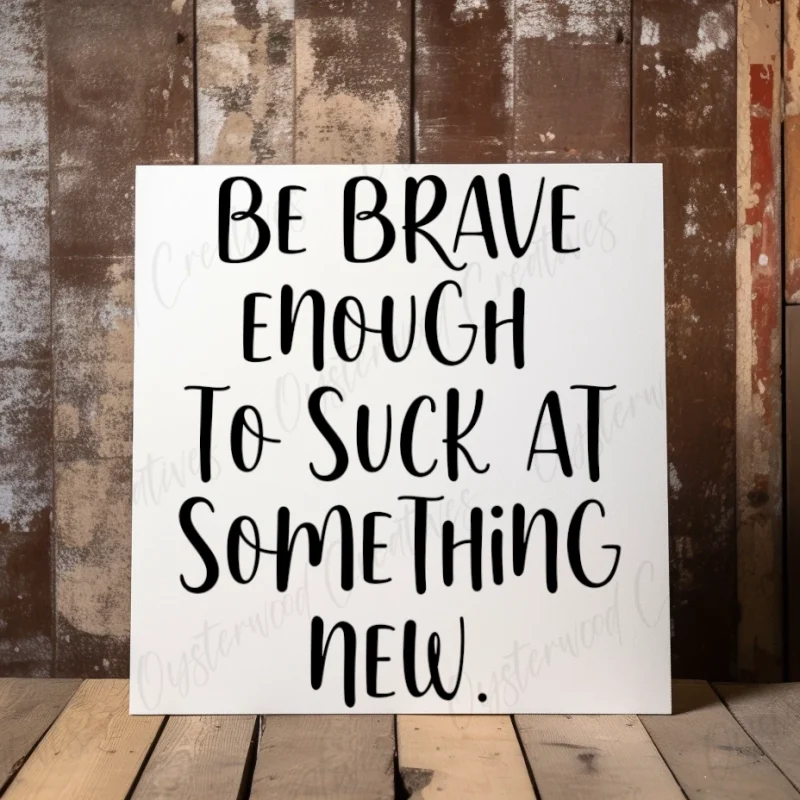 Be brave enough to suck at something new. White sign with black lettering.