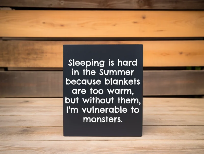 Sleeping is hard in the summer because blankets are too warm, but without them, I'm vulnerable to monsters. Black sign with white lettering.