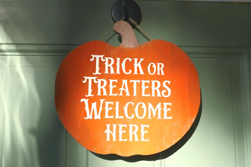 Trick or treaters welcome here. Orange wooden cedar pumpkin hanging on door..